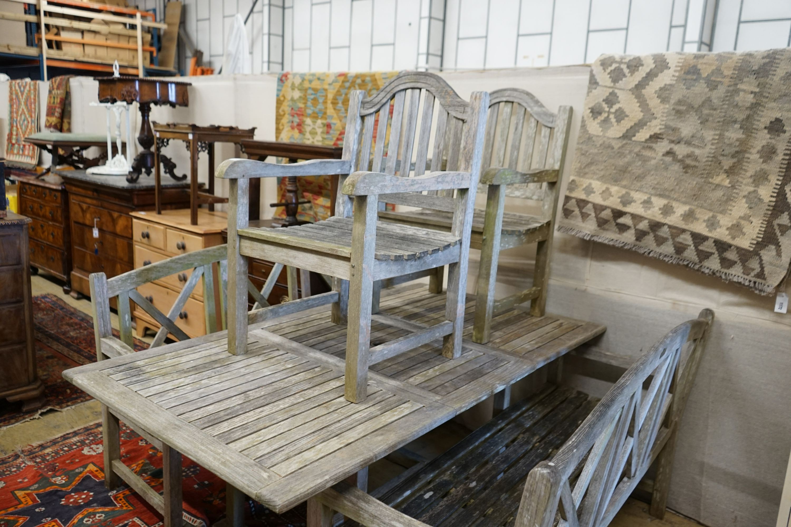 A rectangular weathered teak extending garden table, 180cm extended x 100cm x 74cm, together with a pair of weathered teak garden benches, width 153cm and a pair of teak elbow chairs